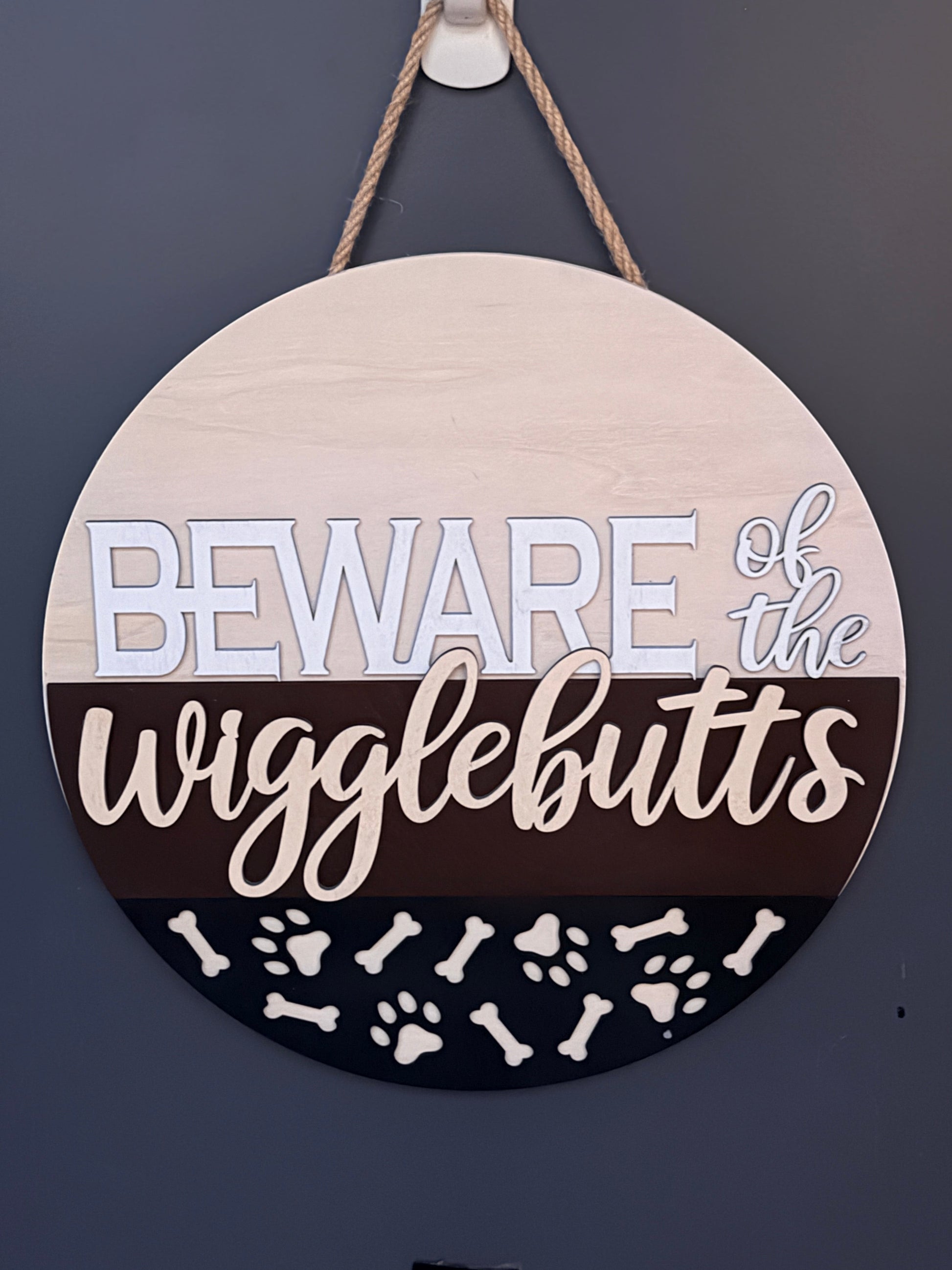 C2 Creative Crafts wooden round hanging sign with "Beware of the wigglebutts" text, paw prints, and bones.
